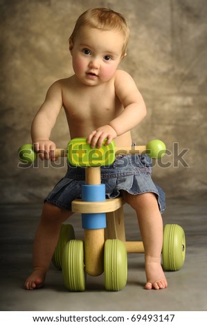 A little blonde girl sitting on a toy bike