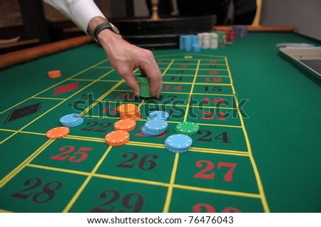 Picture of a hand betting with green, orange and blue chips