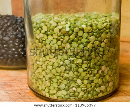 Dried split green peas in an antique jar, with black beans behind