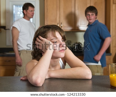 Unhappy family: father and older brother look on as younger brother looks annoyed, tired, bored.