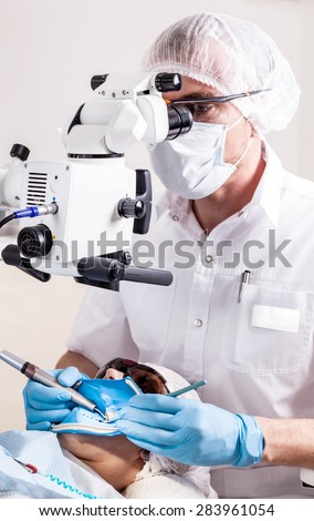 Doctor dentist using dental microscope in modern dental office for operation of a woman patient -Dentistry