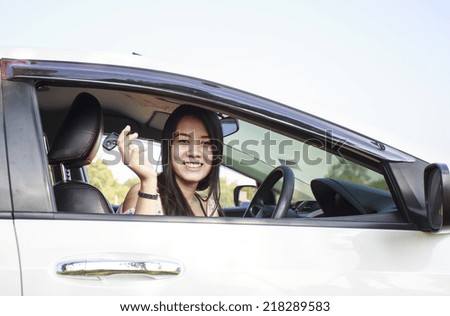 Asian car driver woman smiling showing new car keys and car. Mixed-race Asian and Caucasian girl.