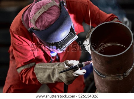 Welder in factory with protective equipment welding pipe