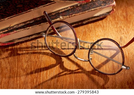 Spectacles with long shadow and some vintage books on wooden surface
