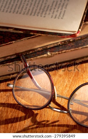 Closeup of spectacles and old books lying on a wooden table with long shadows