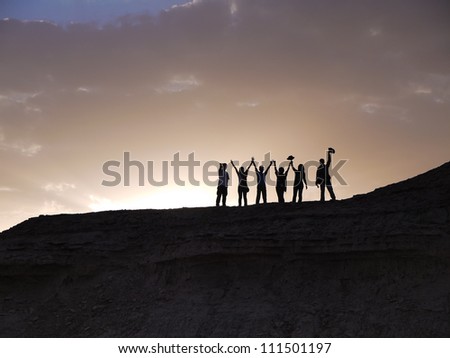 Group of people waving silhouettes against sunset in the desert