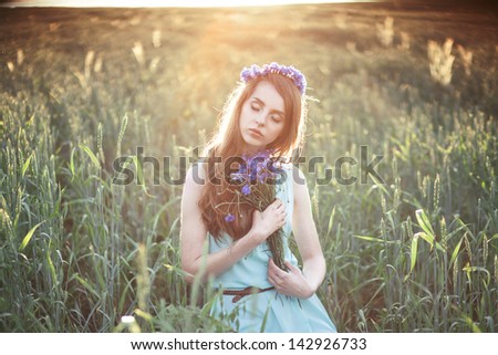 girl in a field in the setting sun with a bouquet of cornflowers