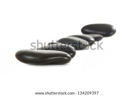 Black massage stones in a row, depth of field, isolated on white background.