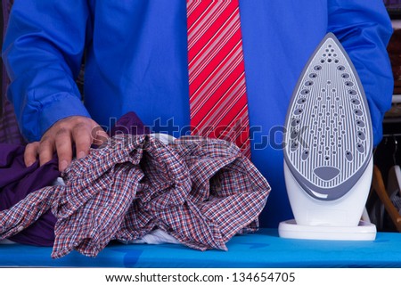 Businessman with red tie and blue shirt holding iron near wrinkle clothes against wardrobe.