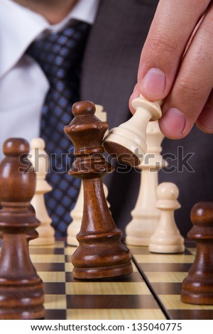 Businessman holding pawn, hitting and defeating opponent king on chess board.