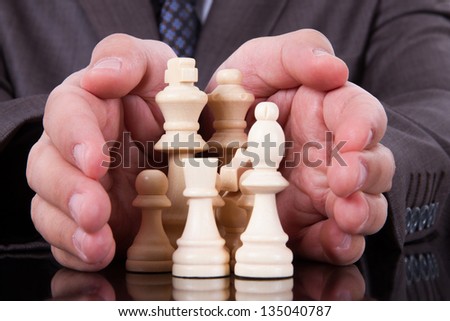 Businessman covers chess pieces on dark table with his hands.