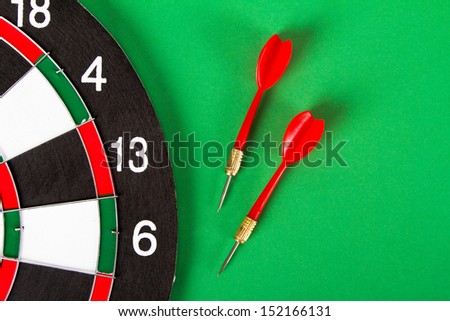 Dart board with black and white sections and red, plastic arrows on green background.