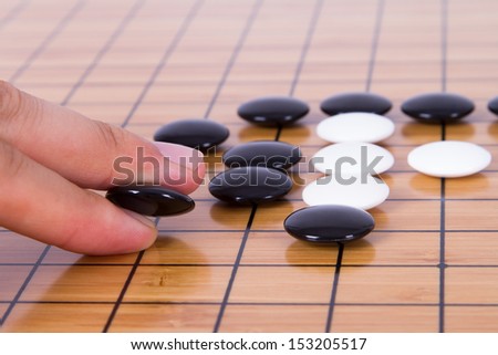 Close up view of hand playing black and white stone pieces on Chinese go game board.
