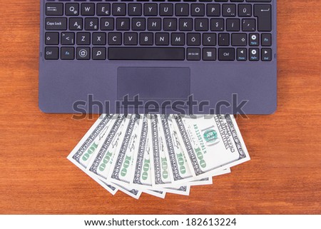 Detail view of laptop and one hundred dollar banknotes on wooden table.