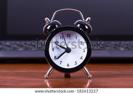 Time concept, alarm clock and laptop on wooden table.