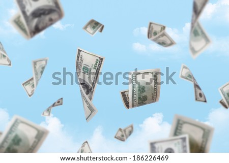Dollar banknotes falling down with depth of field on cloudy sky background.