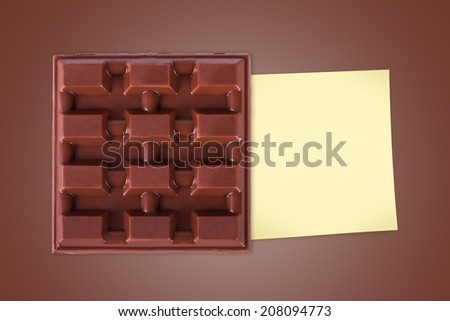 Top view of full milk bar chocolate with sticky note paper for your message on brown background.