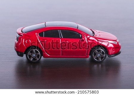 Side view of red, toy, small car on wooden table.