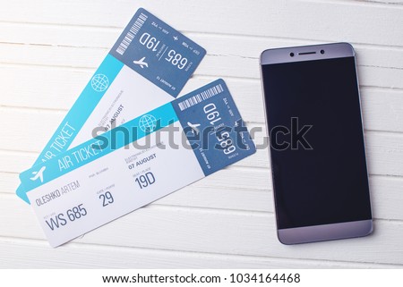 Two tickets are on the table with a phone and laptop. The concept of buying the online ticket booking for travel