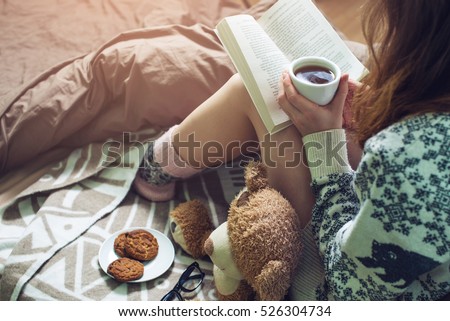 girl reading book in bed with a sweater and warm socks keeping your coffee in hand in the morning. the concept of new year mood.