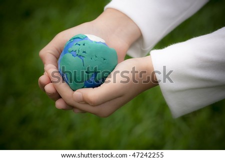 Closeup of child holding plasticine model of Earth in hands, green nature background