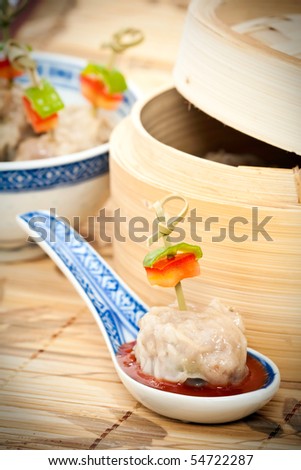 Traditional Chinese meal of dim sum or steamed dumplings on decorative spoon with harissa sauce and bamboo steamer