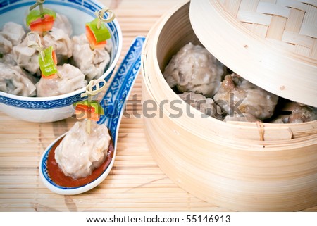 Traditional Chinese meal of dim sum or steamed dumplings on decorative spoon with harissa sauce and bamboo steamer