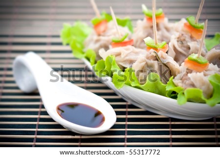 Closeup of Chinese steamed dumplings with a complementary sauce on a ceramic spoon on a bamboo mat nearby.