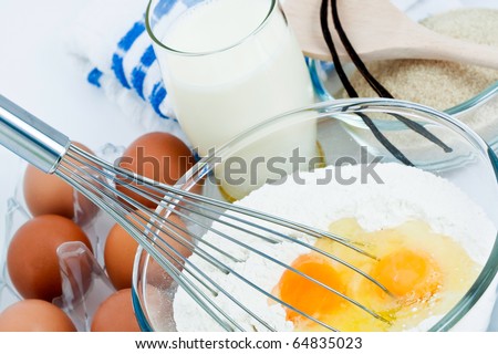 Eggs and flour in bowl with whisk and other ingredients to make pastry.