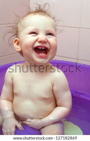 Small smiling baby girl washes in a baby bath with water spray
