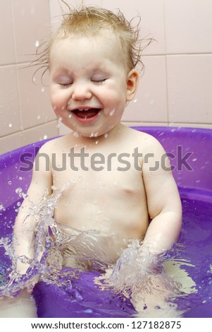 Small smiling baby girl washes in a baby bath with water spray