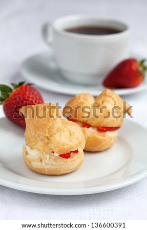Fresh cream puff with whipped cream and strawberries on white plate and cup of coffee on white wooden table