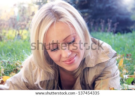 Portrait of beautiful smiling girl with blond hair which lies on sunny meadow with autumn leaves