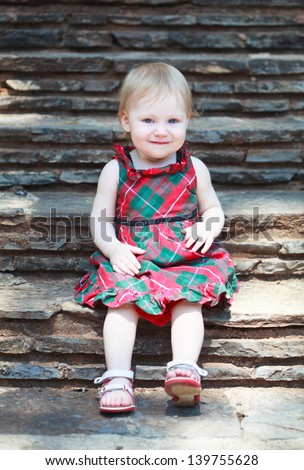Little cute girl in a bright dress sitting on the stairs with stone steps, selective focus on face