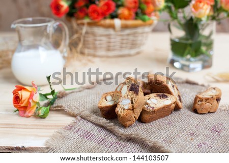 traditional Italian biscotti cookies with almonds and chocolate, bouquet of roses in basket and jar of milk, selective focus