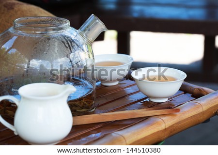 Traditional Chinese tea ceremony accessories, tea leaves in boiling water in a glass pot and cups, selective focus on cup