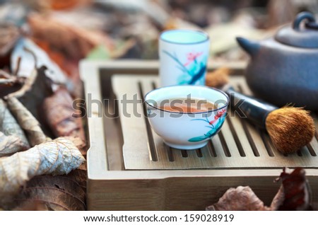Traditional chinese tea ceremony accessories (tea pot and tea pair) on the tea table amongst autumn leaves, selective focus on the cup, copyspace