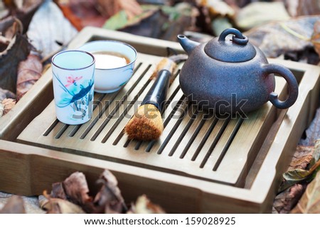 Traditional chinese tea ceremony accessories (tea pot and tea pair) on the tea table amongst autumn leaves, selective focus on the teapot