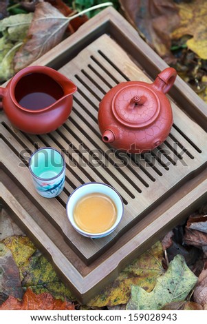 Traditional chinese tea ceremony accessories (tea pot and tea pair) on the tea table amongst autumn leaves, selective focus on the cup