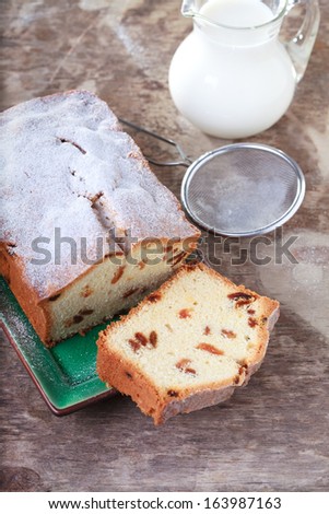 Cake with raisins, sprinkled with powdered sugar and a jug of milk on a wooden table