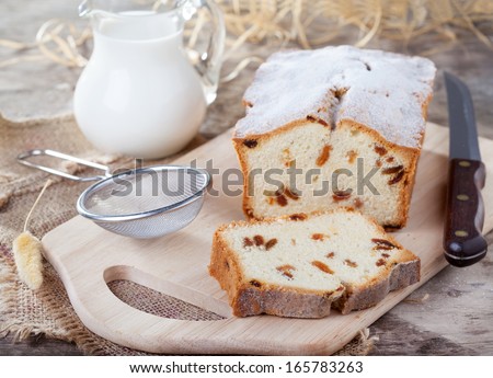 Cake with raisins, sprinkled with powdered sugar and a jug of milk on a wooden table, selective focus on piece of cake