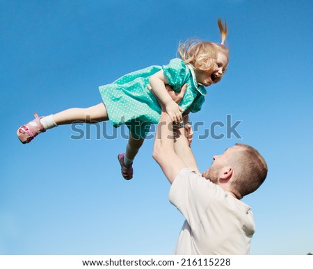 Dad playing with his baby daughter in a blue dress, throws her over his head, selective focus