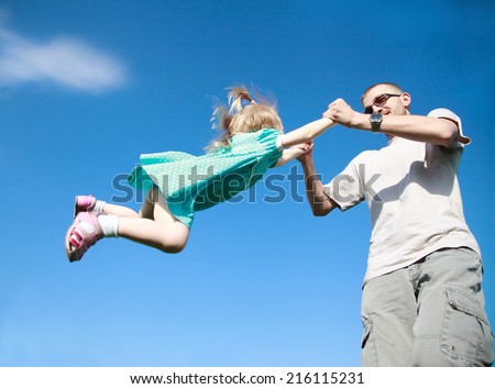 Dad playing with his baby daughter in a blue dress, he turns her around himself at arm\'s length, selective focus, the effect of motion