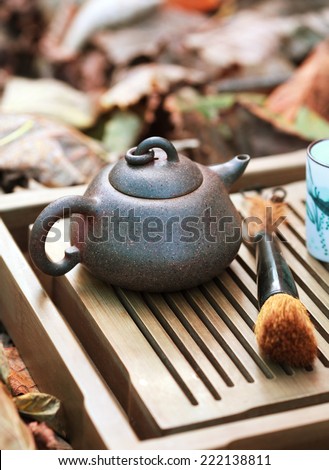 Traditional chinese tea ceremony accessories (tea pot and tea pair) on the tea table amongst autumn leaves, selective focus on the teapot. Toned