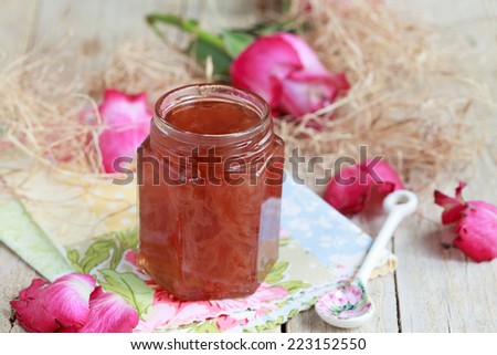 Jar of rose petal jam on a wooden table with flowers roses, selective focus