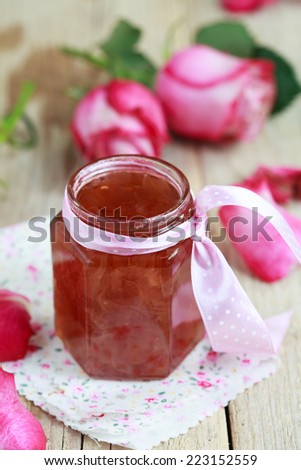 Jar of rose petal jam on a wooden table with flowers roses, selective focus