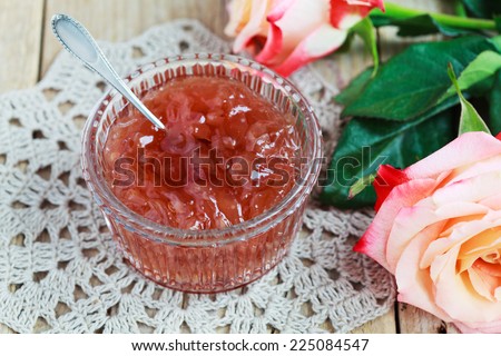 Small jam dish with rose petal jam on a wooden table with flowers roses, selective focus