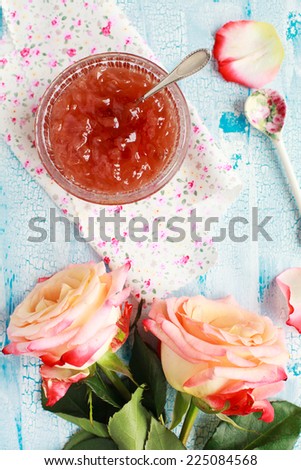 Small jam dish with rose petal jam on a blue wooden table with flowers roses, selective focus