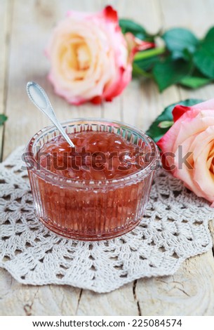 Small jam dish with rose petal jam on a wooden table with flowers roses, selective focus