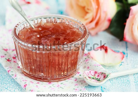 Small jam dish with rose petal jam on a blue wooden table with flowers roses, selective focus